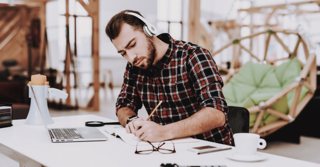 Person at desk listening to headphones and writing
