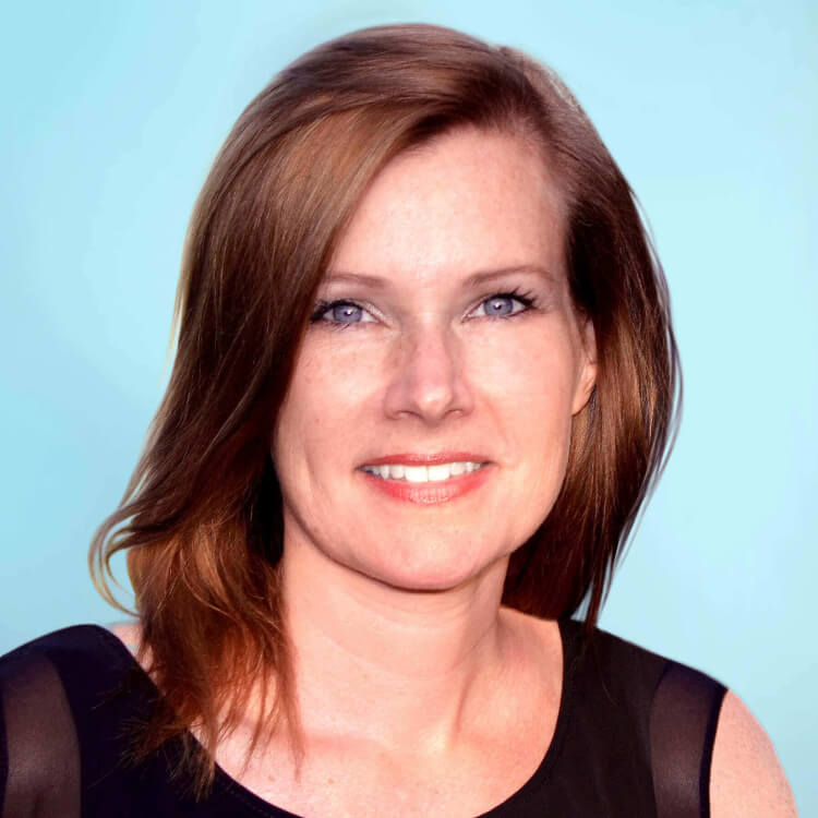 A woman with fair skin and straight, shoulder-length brown hair smiles slightly at the camera. She is wearing a sleeveless black top and is posed against a light blue background.